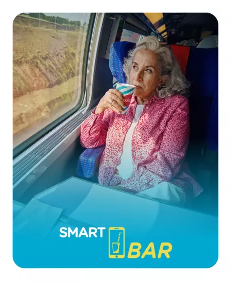 Una mujer sonríe mientras toma un café en el vagón SmartBar de un tren OUIGO.